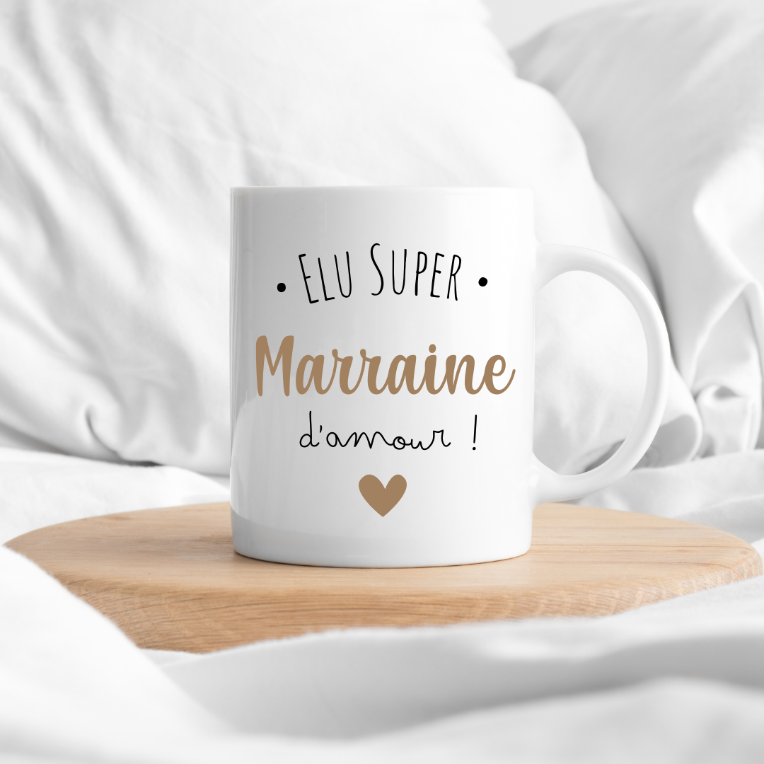 Mug "Élue Super Marraine" dans une jolie boîte cadeau entourée de rubans colorés.
