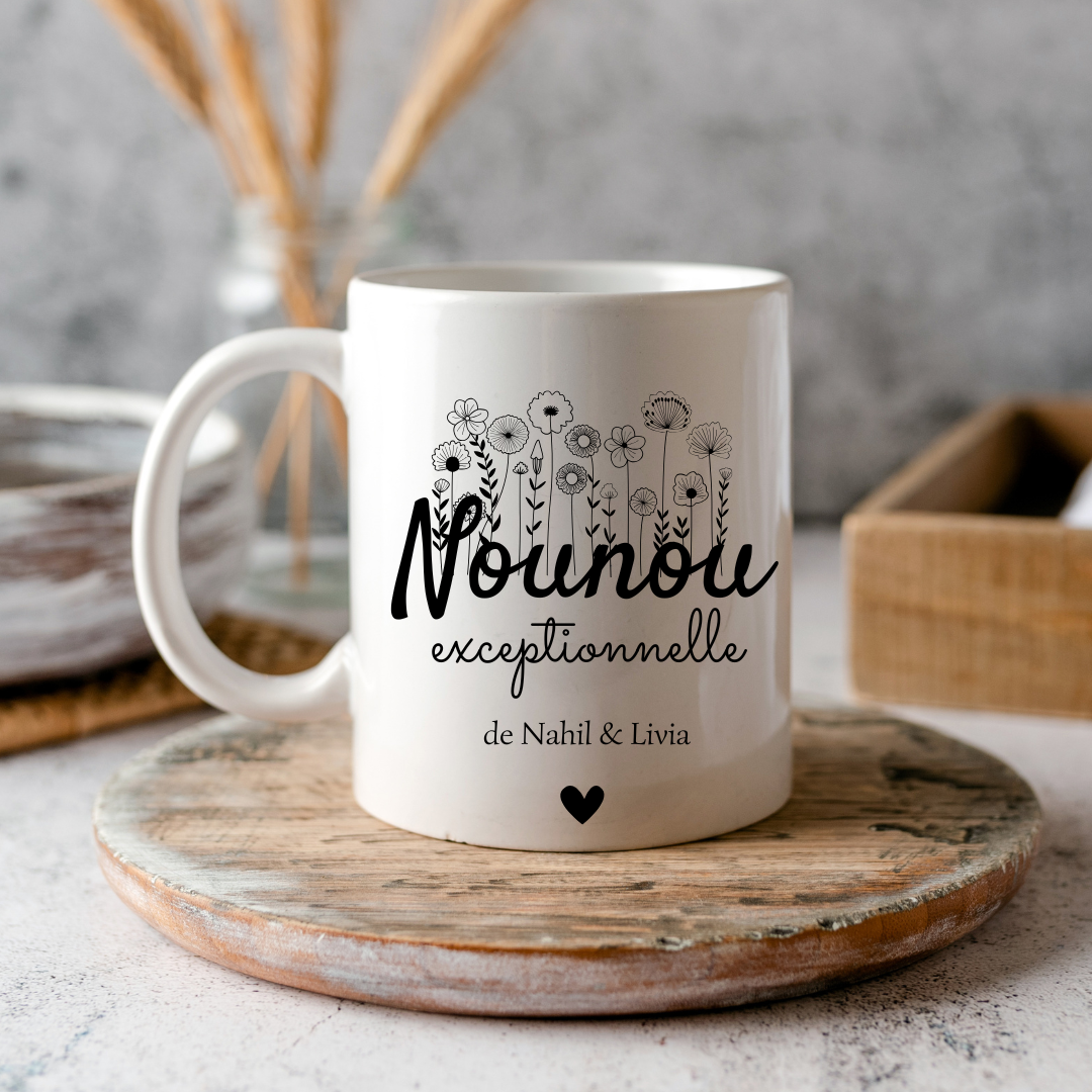  Mug blanc avec l’inscription "nounou Exceptionnelle" et le prénom "Lucas" posé sur une table entourée de fournitures scolaires.