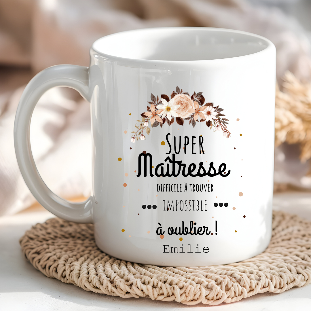  Mug blanc avec l’inscription "Super Maîtresse – Difficile à trouver, impossible à oublier" posé sur un bureau avec des fournitures scolaires.